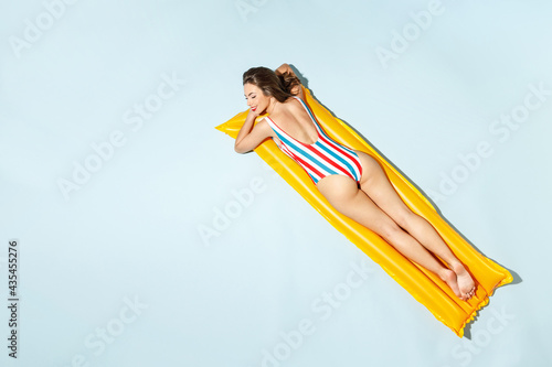 Top back rear view young sexy woman slim body wear striped one-piece swimsuit lies on inflatable mattress hotel pool isolated on pastel blue color background. Summer vacation sea rest sun tan concept. © ViDi Studio