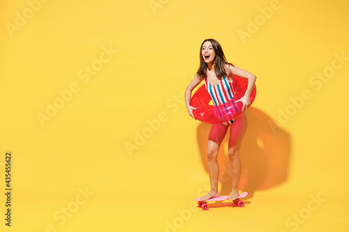 Full length happy young sexy woman slim body wear red blue swimsuit posing with inflatable ring skate isolated on vivid yellow color wall background studio. Summer hotel pool sea rest sun tan concept.