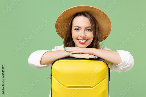 Close up traveler tourist woman in casual clothes hat leaning on yellow suitcase valise look camera isolated on green background Passenger travel abroad weekends getaway Air flight journey concept