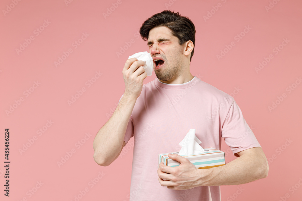 Sick unhealthy ill allergic man has red watery eyes runny stuffy sore nose suffer from allergy trigger symptom hay fever hold paper napkin handkerchief isolated on pastel pink color background studio - obrazy, fototapety, plakaty 