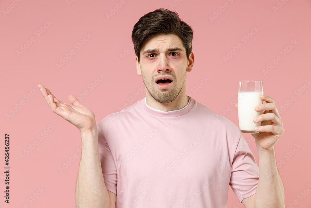 Sick sad unhealthy ill allergic man has red watery eyes, runny stuffy sore nose suffer from intolerance lactose allergy trigger symptom hold milk glass isolated on pastel pink color background studio Sick sad unhealthy ill allergic man has red watery eyes, runny stuffy sore nose suffer from intolerance lactose allergy trigger symptom hold milk glass isolated on pastel pink color background studio