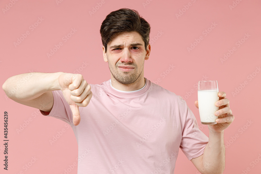 Sick sad unhealthy ill allergic man has red watery eyes, runny stuffy sore nose suffer from intolerance lactose allergy trigger symptom hold milk glass isolated on pastel pink color background studio Sick sad unhealthy ill allergic man has red watery eyes, runny stuffy sore nose suffer from intolerance lactose allergy trigger symptom hold milk glass isolated on pastel pink color background studio