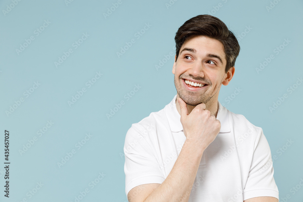 Young pensive dreamful unshaven cheerful caucasian man 20s wearing white casual basic t-shirt prop up chin look aside isolated on pastel blue color background studio portrait People lifestyle concept Young pensive dreamful unshaven cheerful caucasian man 20s wearing white casual basic t-shirt prop up chin look aside isolated on pastel blue color background studio portrait People lifestyle concept