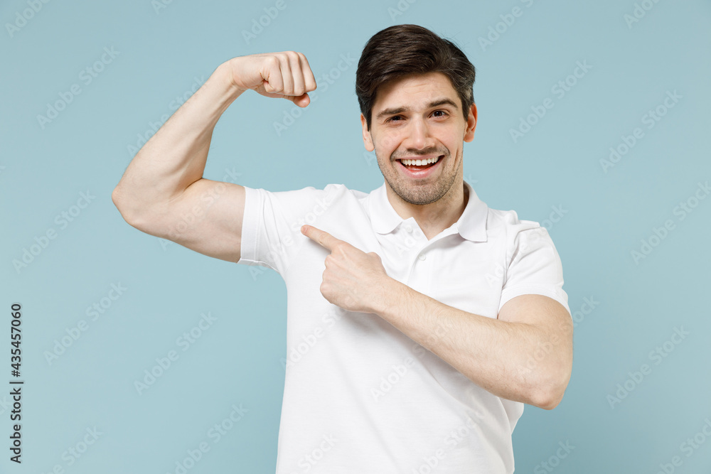 Young unshaven man 20s wear white casual basic t-shirt point finger on biceps muscles demonstrating strength power isolated on pastel blue color background studio portrait People lifestyle concept. Young unshaven man 20s wear white casual basic t-shirt point finger on biceps muscles demonstrating strength power isolated on pastel blue color background studio portrait People lifestyle concept.