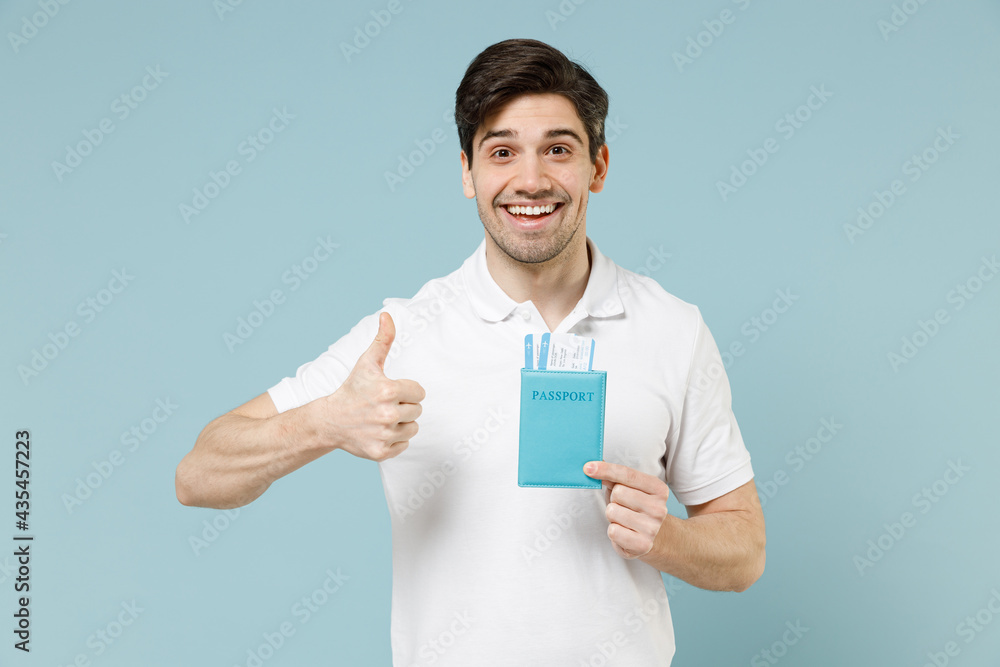 Traveler tourist woman in casual white t-shirt hold passport tickets show thumb up gesture isolated on pastel blue background. Passenger travel abroad on weekends getaway. Air flight journey concept. Traveler tourist woman in casual white t-shirt hold passport tickets show thumb up gesture isolated on pastel blue background. Passenger travel abroad on weekends getaway. Air flight journey concept.