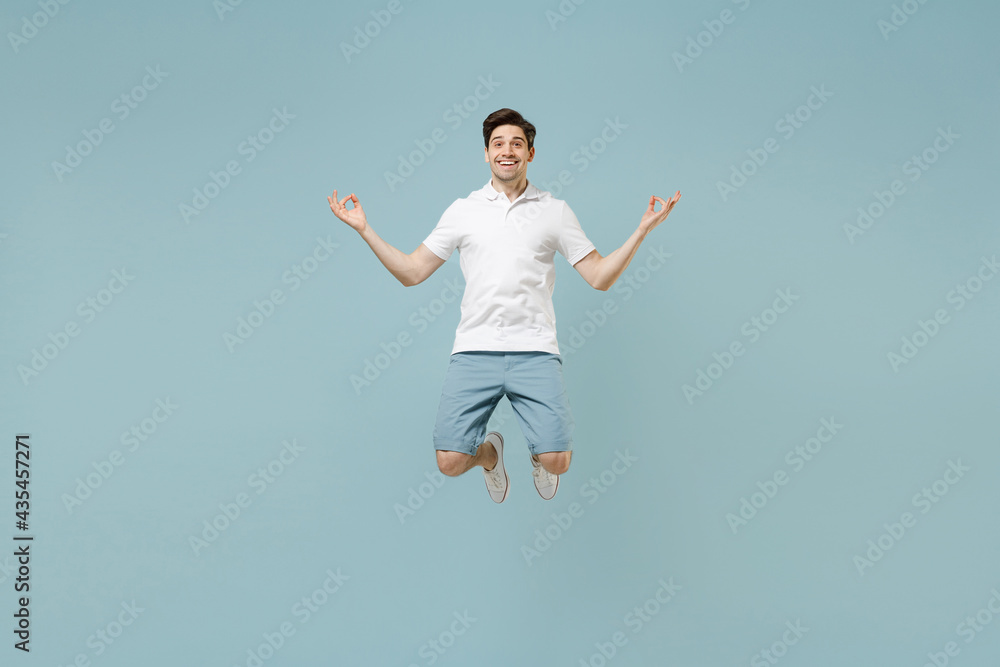 Full size young caucasian man 20s in white casual basic t-shirt hold spread hand in yoga om aum gesture relax meditate try to calm down jump high levitating isolated on pastel blue background studio Full size young caucasian man 20s in white casual basic t-shirt hold spread hand in yoga om aum gesture relax meditate try to calm down jump high levitating isolated on pastel blue background studio