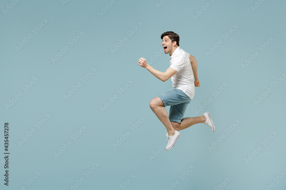 Full length young fun caucasian man 20s wear white casual basic t-shirt run fast jump high with outstretched hands isolated on pastel blue color background studio portrait. People lifestyle concept