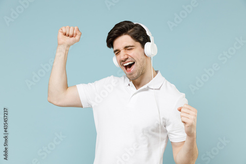 Young fun smiling happy attractive unshaven cheerful caucasian man wear white t-shirt headphones dancing rest in free time isolated on pastel blue background studio portrait. People lifestyle concept. © ViDi Studio