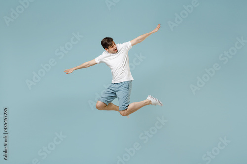 Full length young fun happy european man 20s wearing white casual basic t-shirt jump high with outstretched hands isolated on pastel blue color background studio portrait. People lifestyle concept