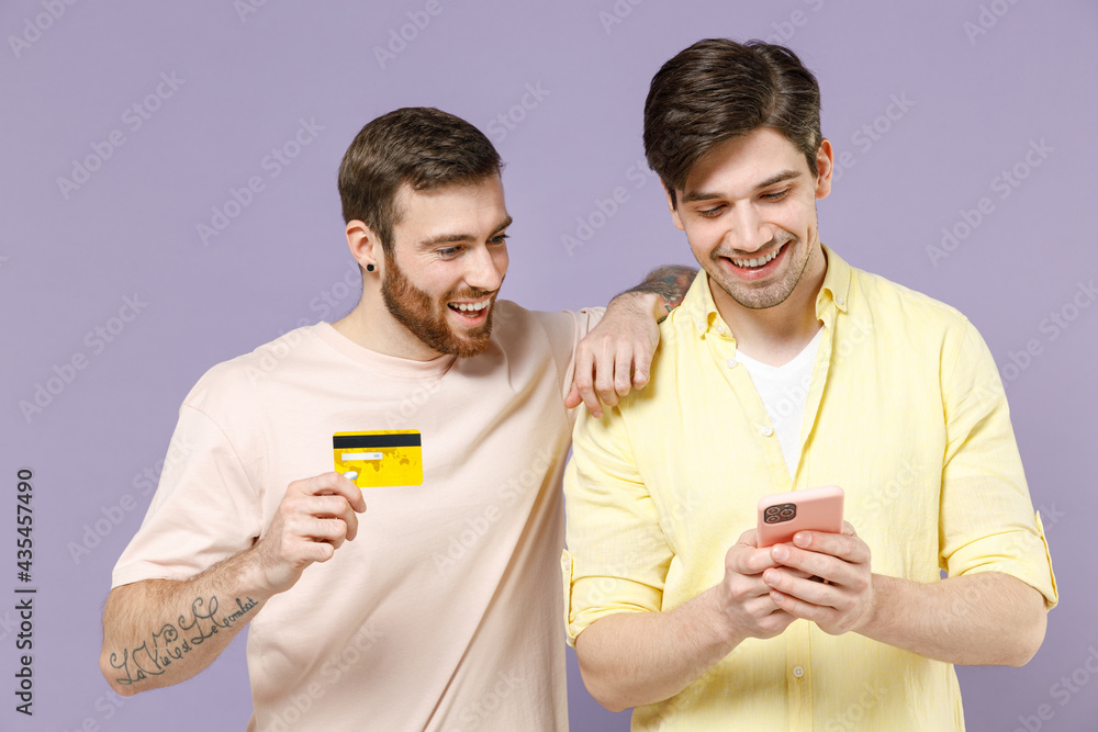 Young cool men friends together wear casual t-shirt tattoo translate fun hold mobile cell phone use credit bank card shopping online isolated on purple background People lifestyle friendship concept