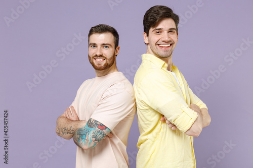 Side view of two caucasian young men friends together in casual t-shirt stand back to back hold hands crossed folded isolated on purple background studio portrait People lifestyle friendship concept. © ViDi Studio