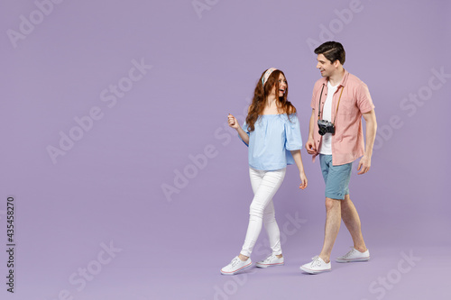 Full length side view two excited traveler tourist woman man 20s couple in summer clothes wlak go isolated on purple background Passenger travel abroad on weekends getaway. Air flight journey concept photo