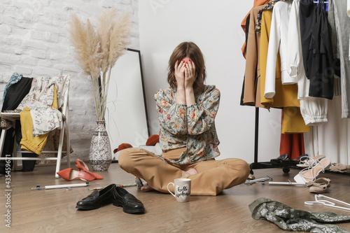Φωτογραφία Stressed young woman sitting in the messy room full of clothes