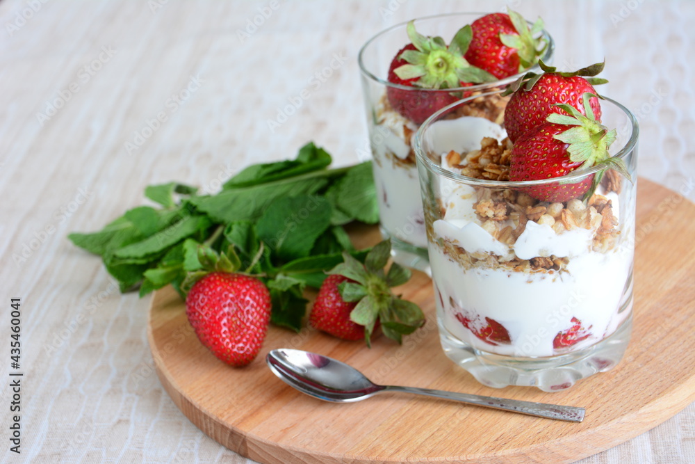 strawberry dessert with yogurt, granola and mint leaves on the cutting board background with a teaspoon and tablecloth strawberry dessert with yogurt, granola and mint leaves on the cutting board background with a teaspoon and tablecloth