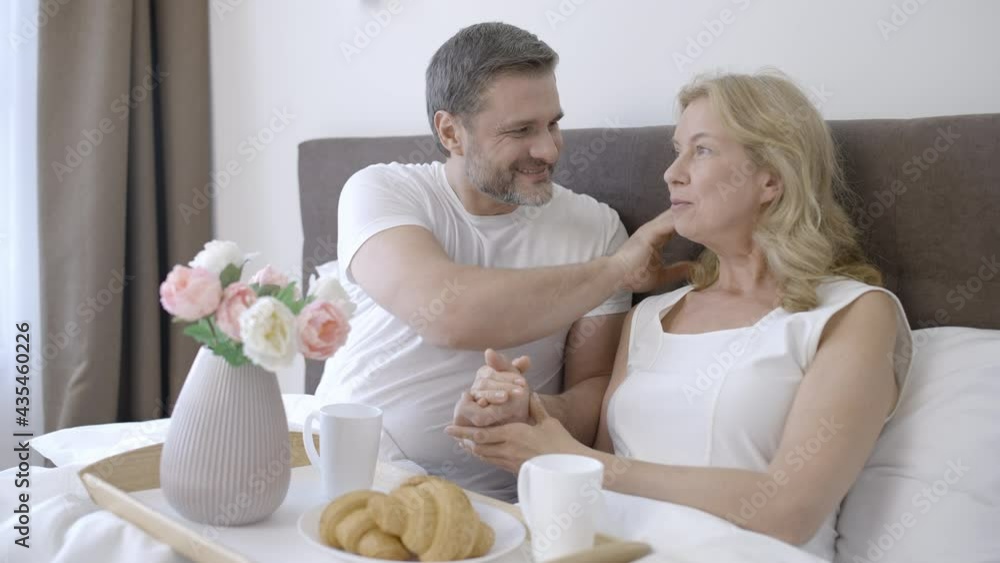Caring male in his 40s talking with loving wife during romantic breakfast in bed Caring male in his 40s talking with loving wife during romantic breakfast in bed