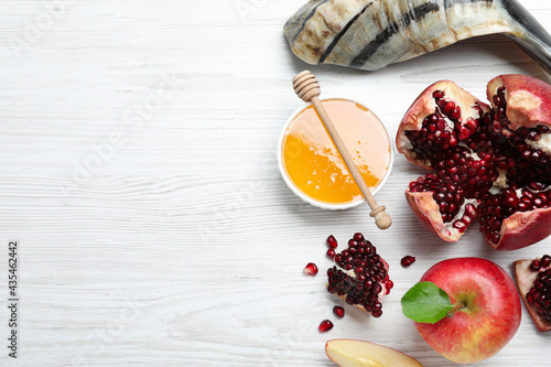 Honey, pomegranate, apples and shofar on white wooden table, flat lay with space for text. Rosh Hashana holiday