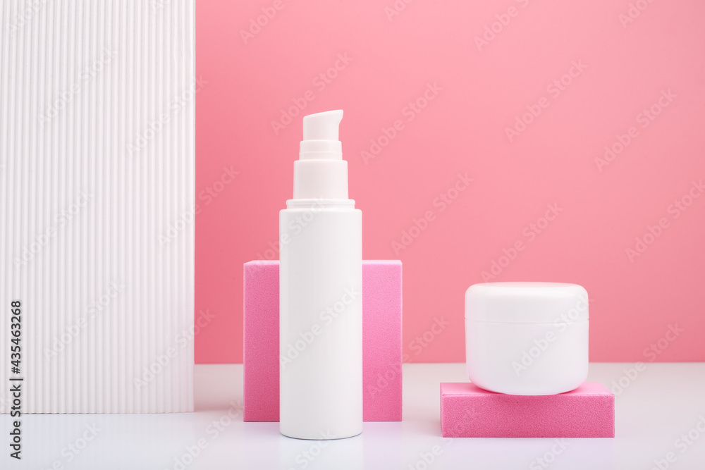 Set of white cosmetic tube and jar with face cream and under eye cream, mask or scrub against bright pink background and white wall with stripes. Set of white cosmetic tube and jar with face cream and under eye cream, mask or scrub against bright pink background and white wall with stripes.