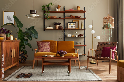Stylish interior of living room with honey yellow sofa, wooden bookcase, plants, commode, picture frame, carpet, decoration and elegant accessoreis in home decor. Template.