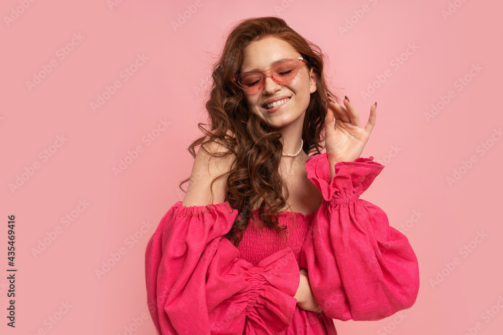 Fashion studio portrait of stylish red-haired woman posing in pink lien dress with sleeves over pink background. Fashion studio portrait of stylish red-haired woman posing in pink lien dress with sleeves over pink background.