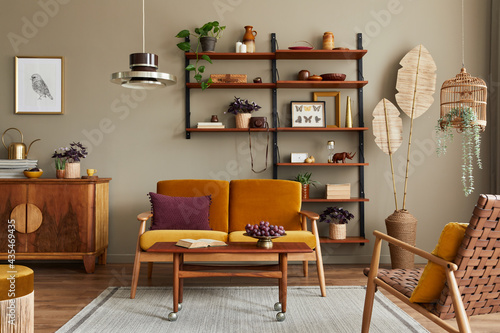 Stylish interior of living room with honey yellow sofa, wooden bookcase, plants, commode, picture frame, carpet, decoration and elegant accessoreis in home decor. Template. © FollowTheFlow