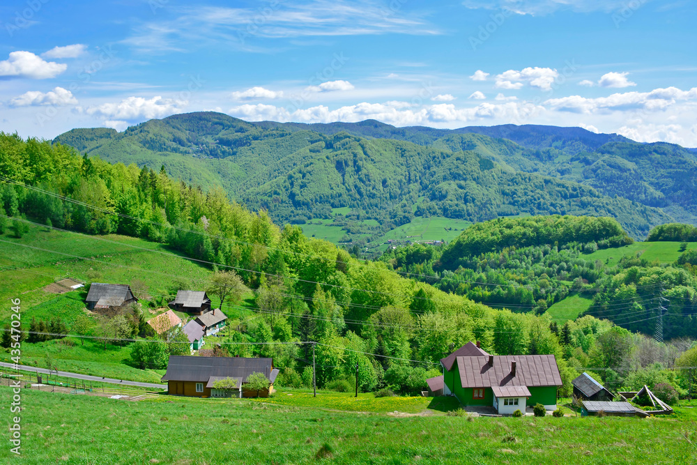  View of the surrounding countryside with hills, houses, meadows  and a forest under a blue sky and mountains range in spring sunny day, Rytro, Poland