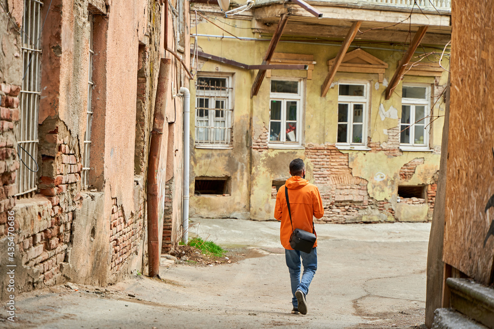 A lonely guy walks in the old part of the city between dilapidated houses