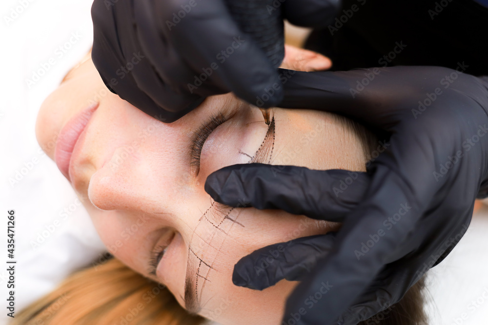 the permanent makeup artist stretches the skin in the area of the eyebrows to perform the tattoo - obrazy, fototapety, plakaty 