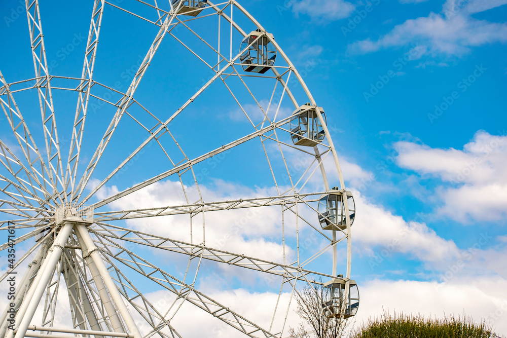 A giant construction of a Ferris wheel against a blue sky with clouds.