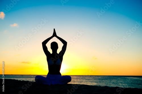 Woman meditating, doing yoga, at the beach, sitting by the seashore, dressed in a white outfit at sunset © TRAVEL EASY