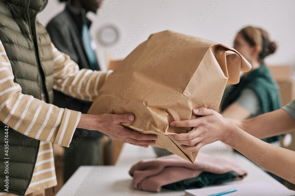 Close up of unrecognizable person giving paper bag to volunteers during help and donations event, copy space Close up of unrecognizable person giving paper bag to volunteers during help and donations event, copy space