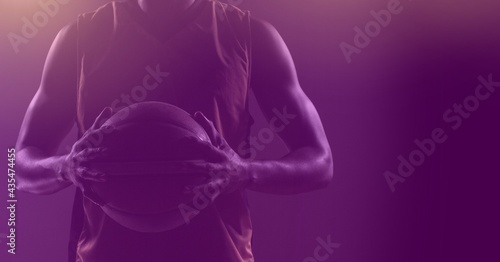 Composition of fit male basketball player holding ball with copy space on purple background