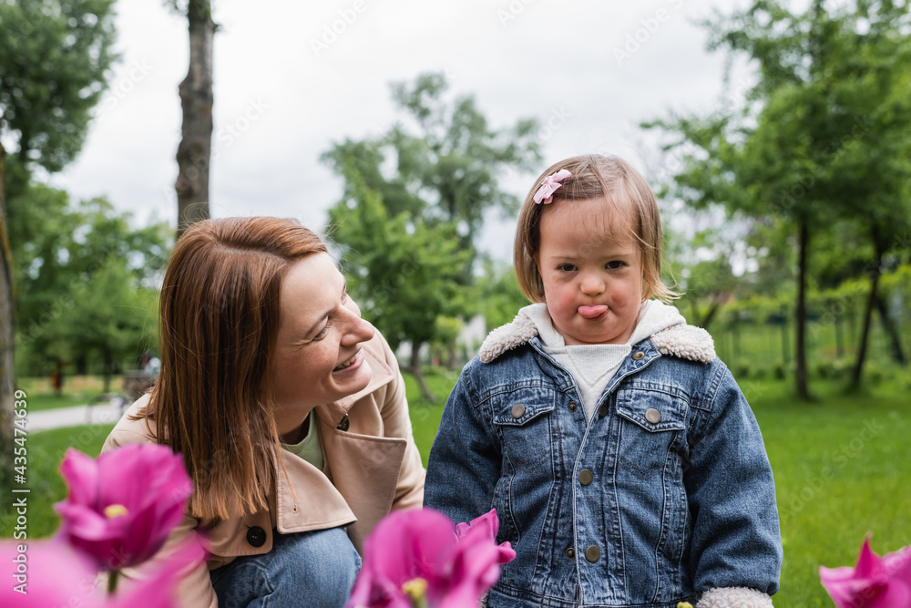happy mother smiling and looking at disabled daughter sticking out tongue happy mother smiling and looking at disabled daughter sticking out tongue