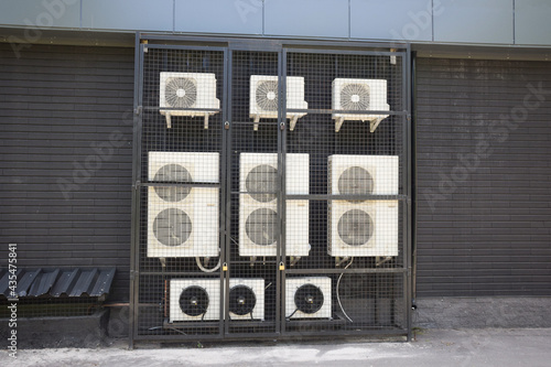 There are many working air conditioners of different types and capacities near the wall of a store or office.