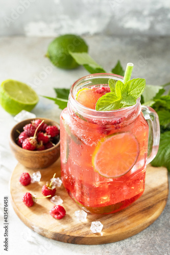 Soft drinks, healthy beverage. Refreshing summer glasses drink raspberry with mint lime and ice on a stone table.