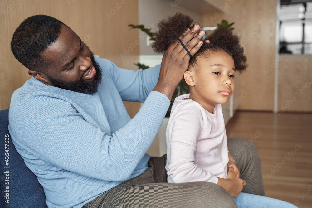 Obraz premium African american father brushing making hairstyle for his young daughter