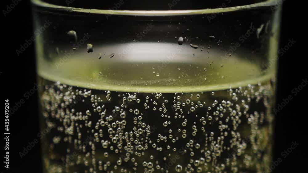Close-up of a glass of sparkling champagne on a black background, small air bubbles slowly rising up. A spotlight illuminates a glass of champagne in the dark. Close-up of a glass of sparkling champagne on a black background, small air bubbles slowly rising up. A spotlight illuminates a glass of champagne in the dark.