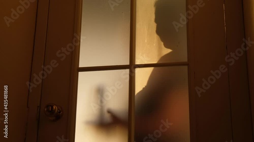 Cruel mother or stepmother screams and brandishes a stick as she breaks into the room, silhouette, view through the glass door