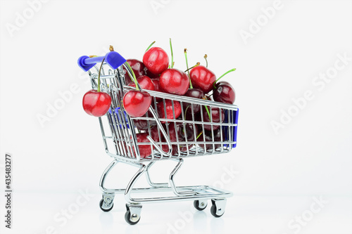 Cherries in shopping cart and on white background. Copy space.