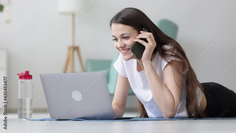 Sport woman on fitness mat at home talking by mobile phone and using laptop computer Spbi. Smiling Sport woman on fitness mat at home talking by mobile phone and using laptop computer Spbi. Smiling