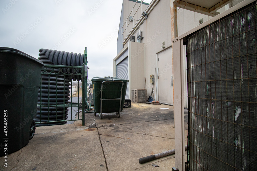 Cart, air conditioner unit, trash bin, with doors behind shopping center building on cloudy day in winter Cart, air conditioner unit, trash bin, with doors behind shopping center building on cloudy day in winter