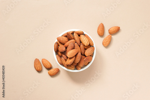 top view of roasted almonds in circle white ceramic bowl placed on brown background.