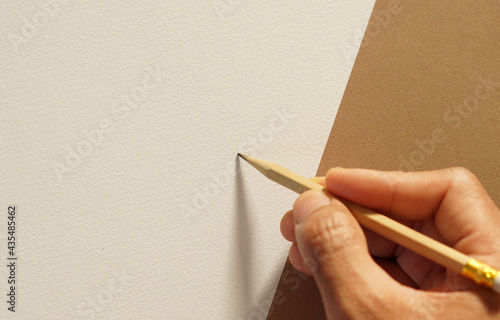 top view of man's right hand was holding a brown wooden pencil, writing on a blank white and brown paper, selective focus at pencil, copy space.