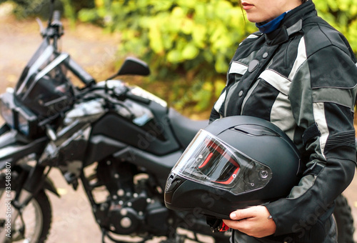 girl motorcyclist holds a protective helmet in her hands on the background of a blurred motorcycle.