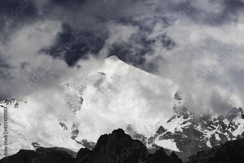 Black and white high snowy mountains with glacier, rocks and sky with gray fog before storm