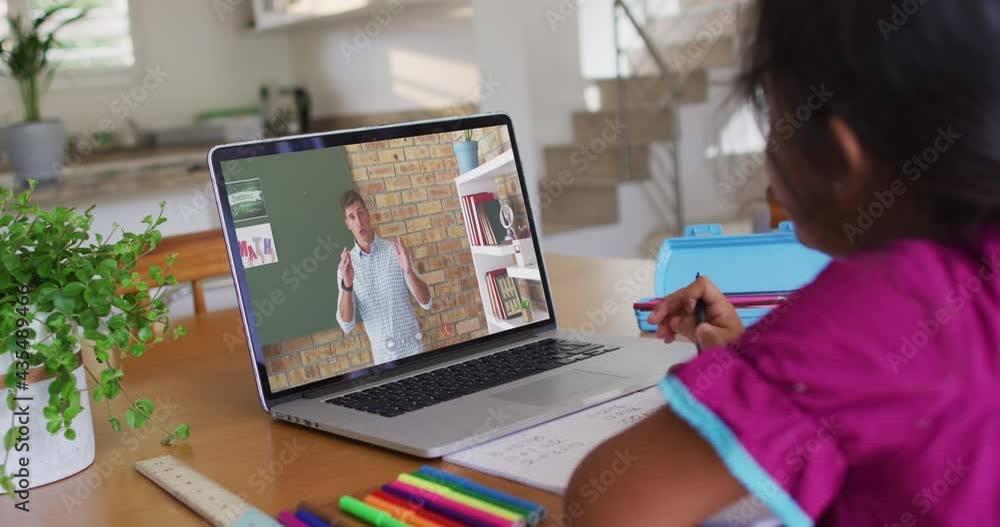 Mixed race girl sitting at desk using laptop having online school lesson Mixed race girl sitting at desk using laptop having online school lesson