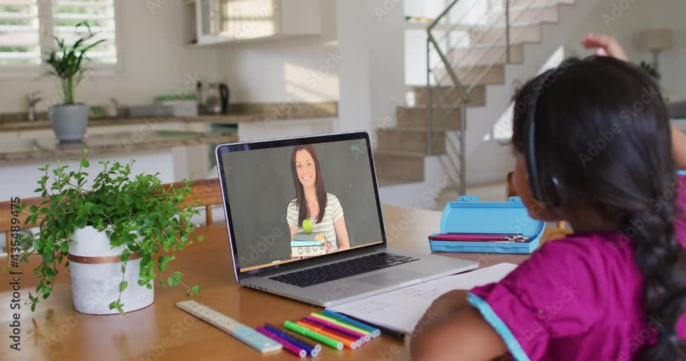 Mixed race girl sitting at desk using laptop having online school lesson Mixed race girl sitting at desk using laptop having online school lesson