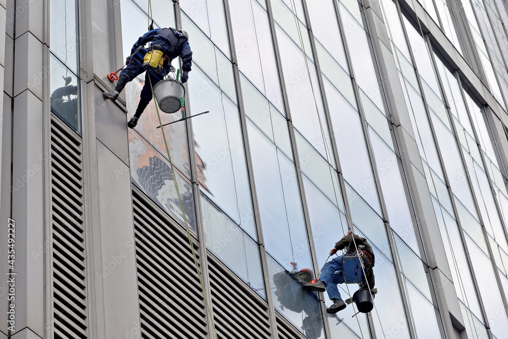 Industrial climber washes glass on the facade of a skyscraper. Industrial mountaineering, high-rise facade cleaning services