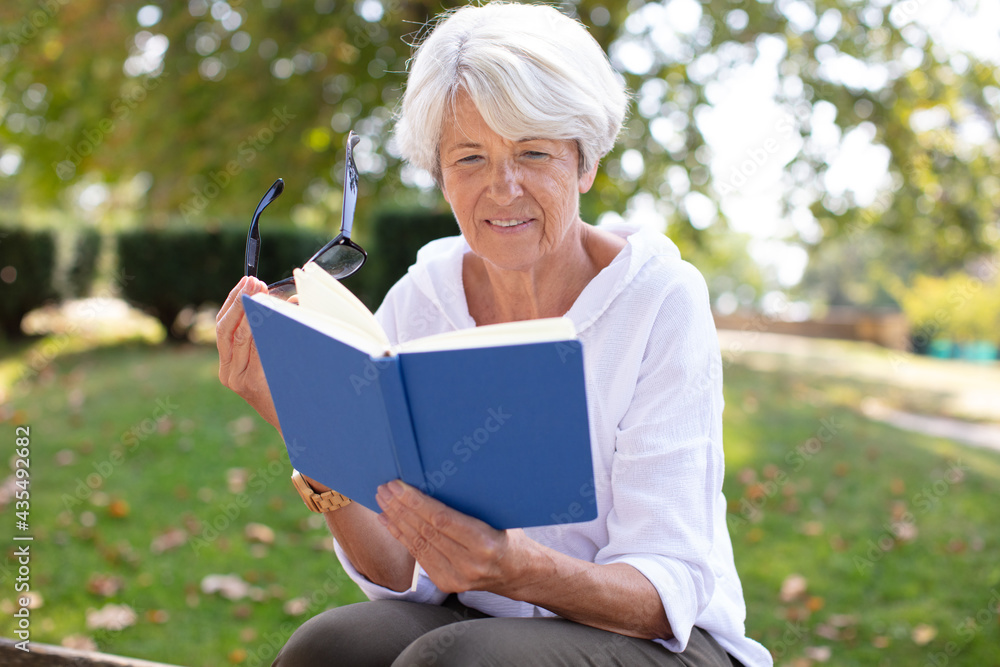 mature blonde woman reading a book in the garden mature blonde woman reading a book in the garden