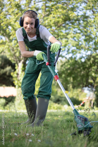 woman gardener in uniform mows the grass trimmer photo