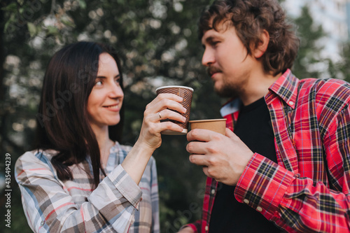 A handsome man and a girl in plaid shirts are resting in nature with hot coffee, tea in an eco-friendly paper cup in their hands. Photography, concept.